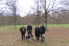Vier Männer stehen auf einer Fläche, auf der verteilt im gleichen Abstand kahle Bäume stehen